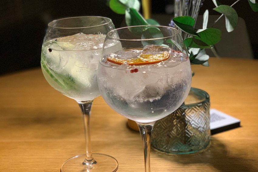 Zwei Gin Tonic Cocktails mit Orangenscheibe auf einem Holztisch bei Kultur Genuss